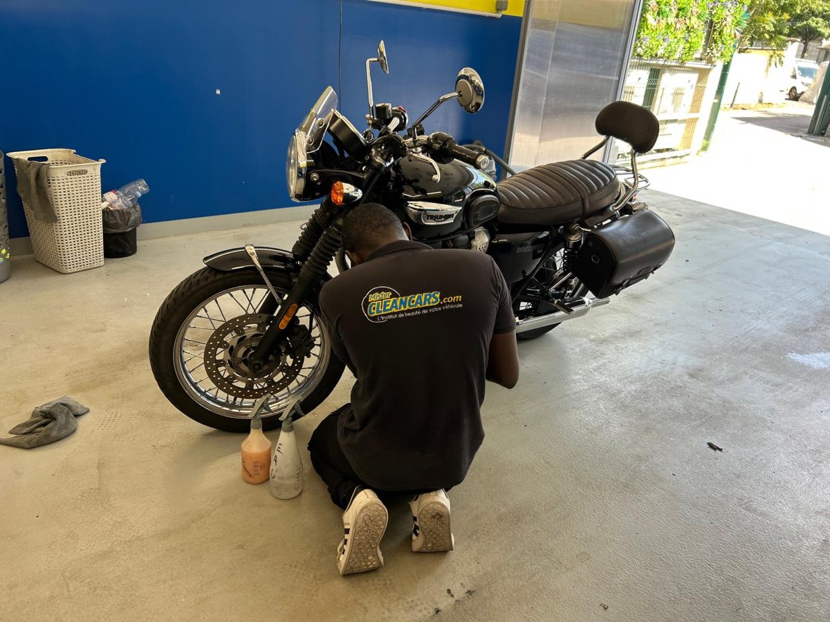 Laveur Mister Clean Cars nettoyant à la main une moto Triumph Bonneville